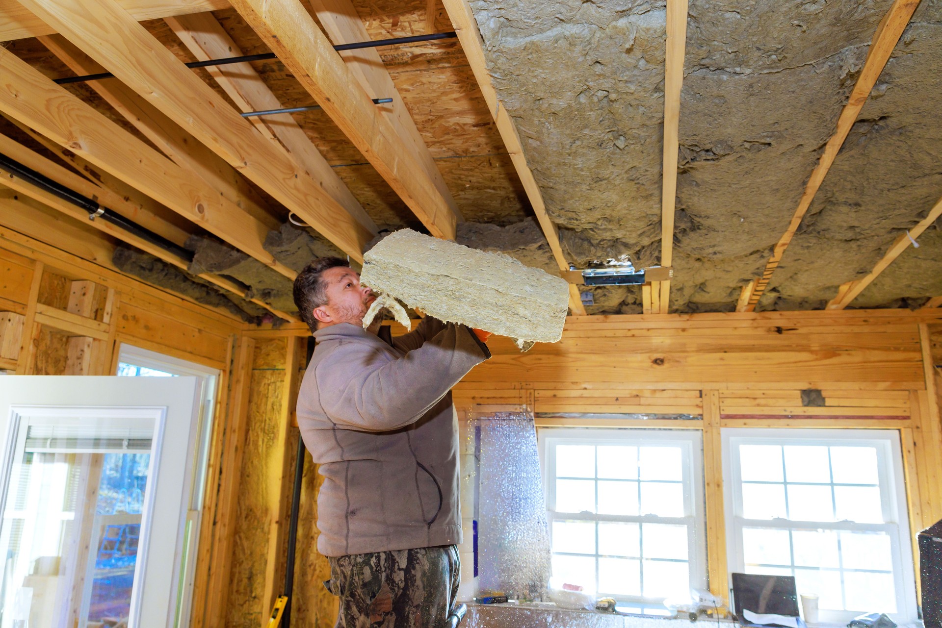 Worker installs insulation material in a wooden house during construction on a winter day Worker installs insulation material in a wooden house during construction on a winter day